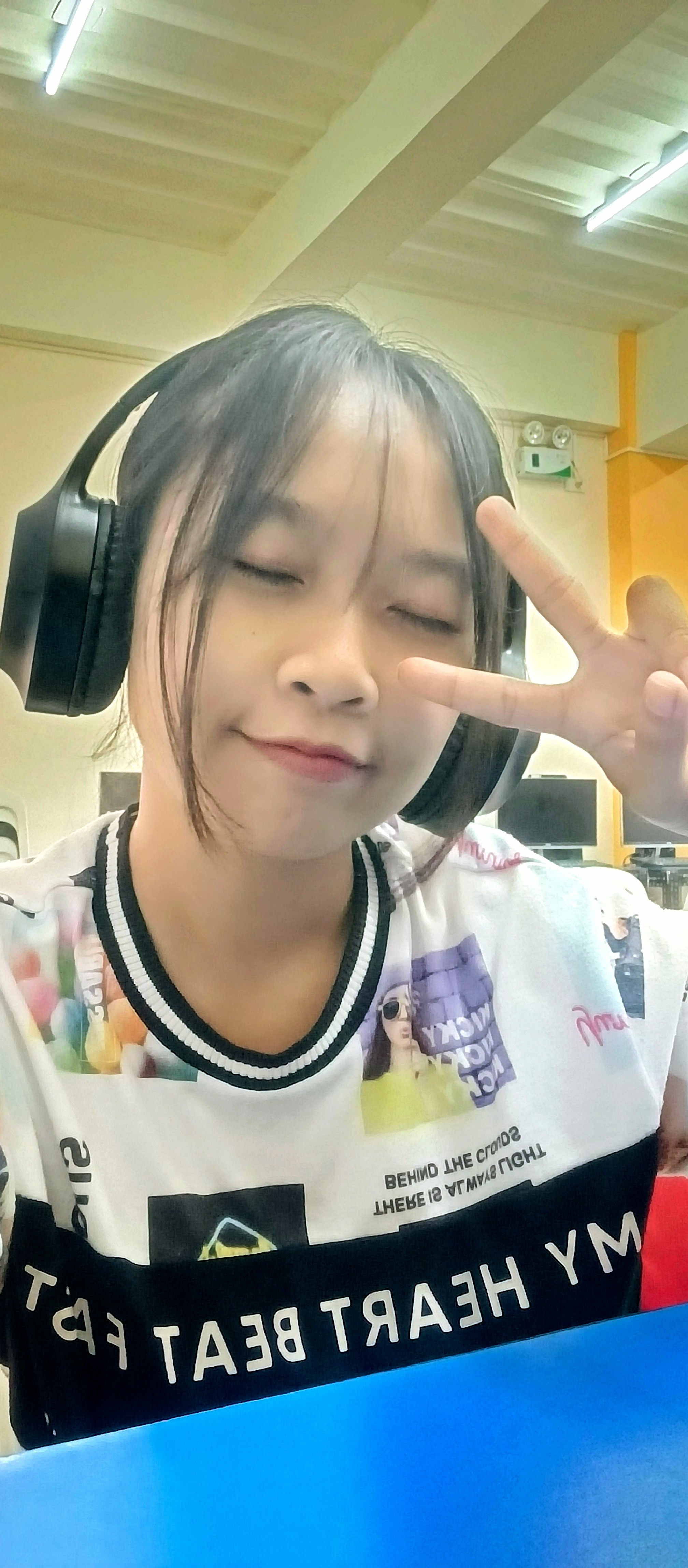 Robel J. Azucena smiling with eyes closed, wearing black headphones and making a peace sign, in a graphic print t-shirt